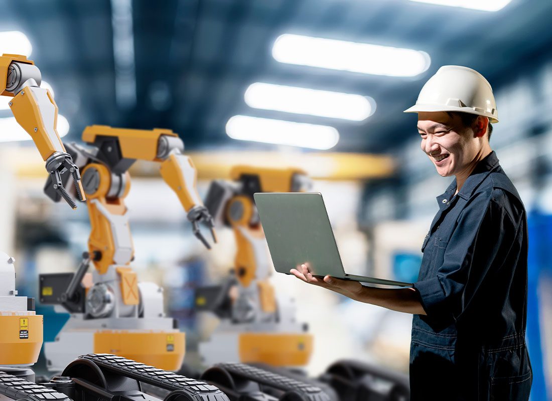 Insurance By Industry - Smiling Engineer Working With Robot Arm Machine in an Industrial Technology Factory Product Line