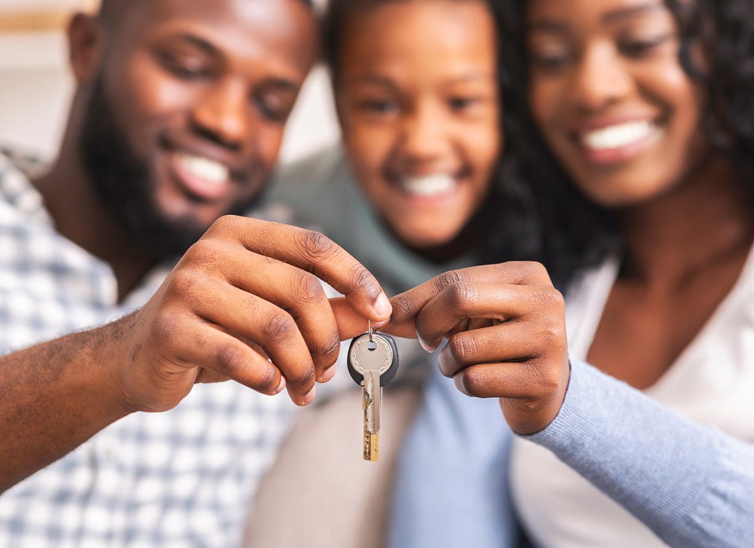 Personal Insurance - Smiling Happy Family Closeup Holding Keys to Their New Home With Focus on Keys and Their Faces Blurred