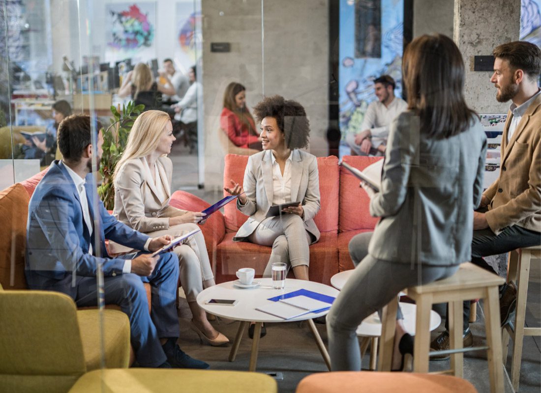 About Our Agency - Portrait of Corporate Office Workers Formally Dressed and Smiling at the Camera During a Conference Meeting With Modern Technologies Surrounding a Circle Table