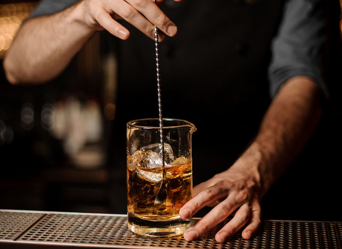 Liquor Liability Insurance - Close-up View of Bartender Stirring Drink with Ice Over an Antique Bar